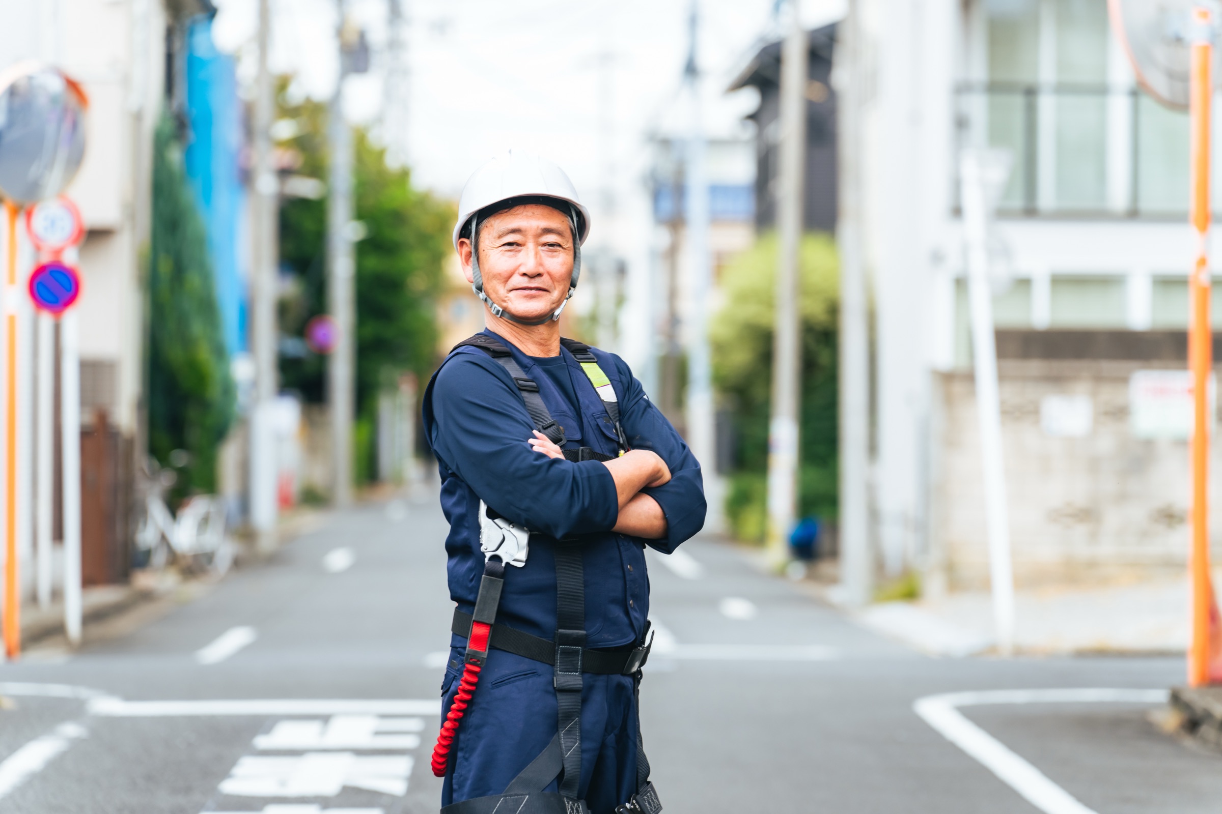白いヘルメットに作業着姿で腕を組んでほほえむ職人
